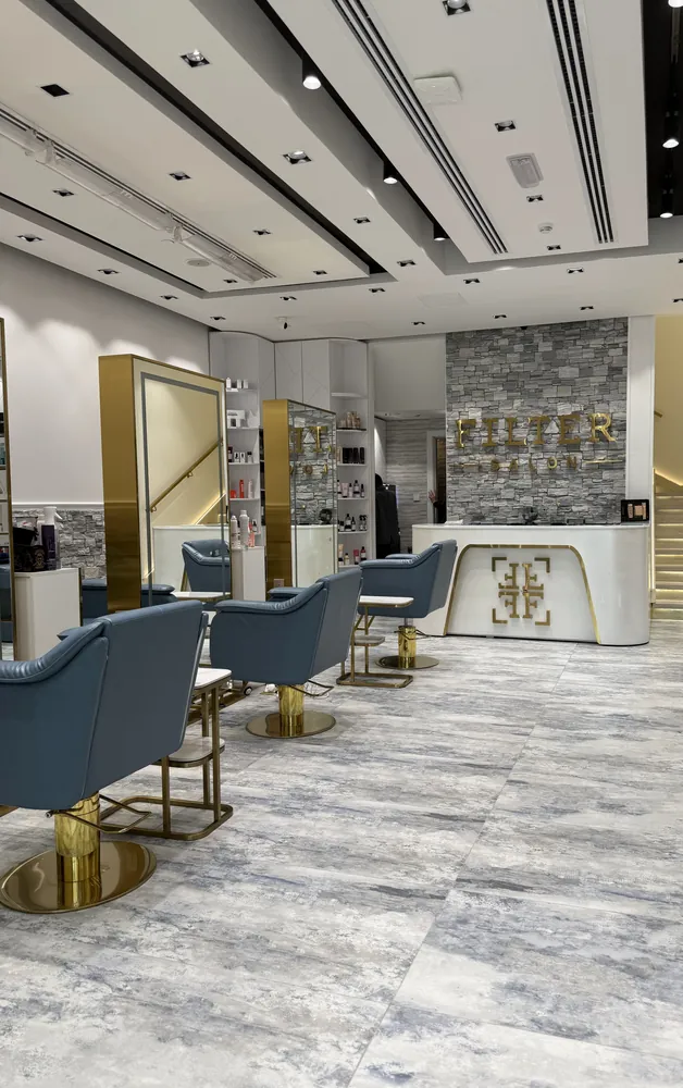 The salon floor at FILTER Al Bateen, Marasy — blue chairs, stone wall and gold lettering — FILTER Ladies Salon Abu Dhabi